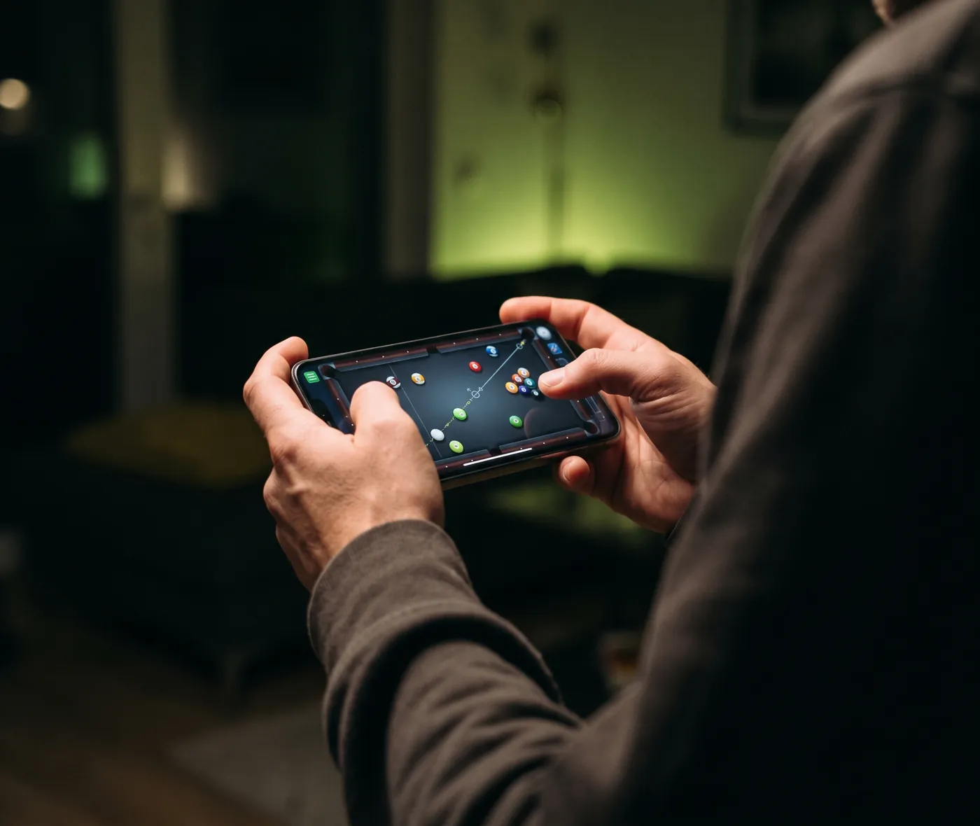 A player holding a phone sideways, lining up a shot in a pool game
